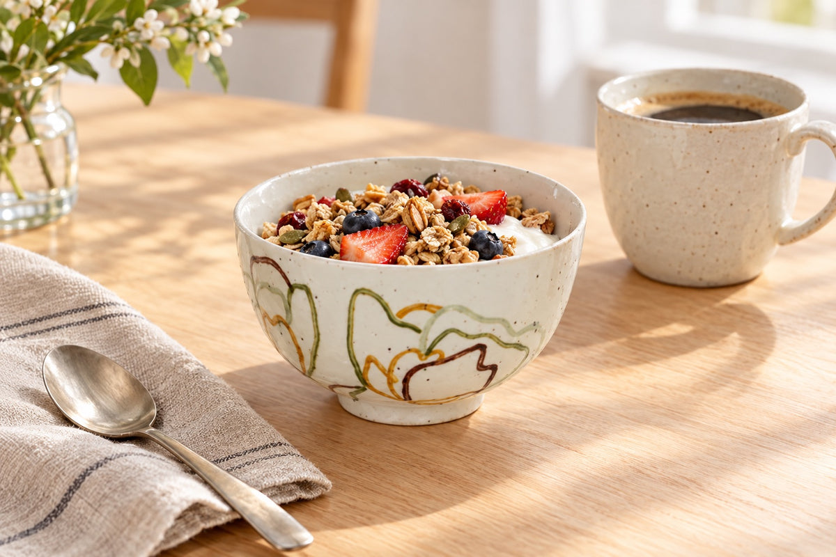 Bol zen blanc en grès à motif floral doré rempli de granola sur une table de petit-déjeuner