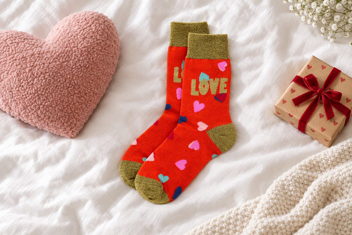 Chaussettes Love rouges à cœurs posées sur un lit avec un coussin