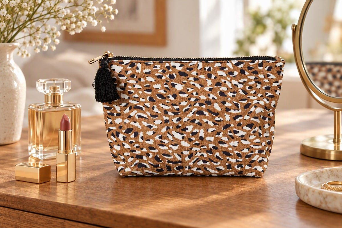 Pochette léopard avec pompon noir posée sur une coiffeuse avec rouge à lèvres et parfum