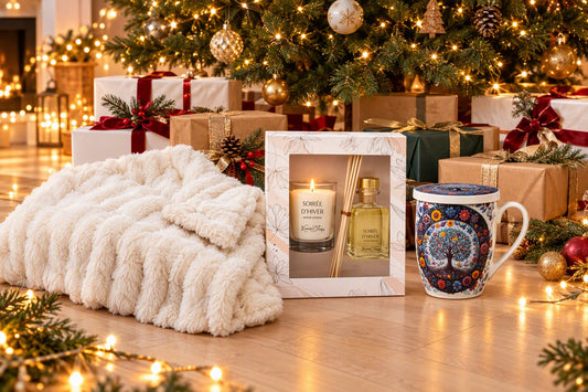 Cadeaux de Noël emballés au pied du sapin avec un plaid nuage crème, un coffret bougie et diffuseur et un mug tisanière déballés