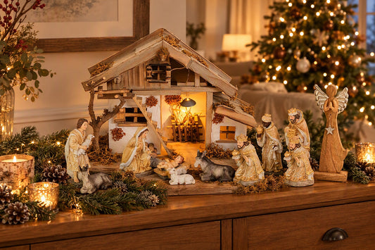 Crèche de Noël lumineuse en bois avec santons beige et or et ange argenté sur un buffet décoré de sapin