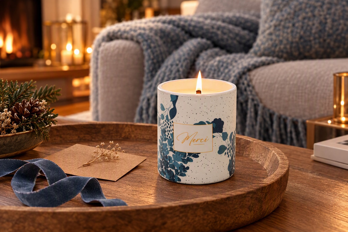 Bougie merci allumée dans un pot en céramique à feuilles bleues sur une table basse