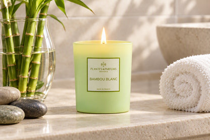 Bougie Bambou blanc allumée dans une salle de bain zen avec tiges de bambou et galets