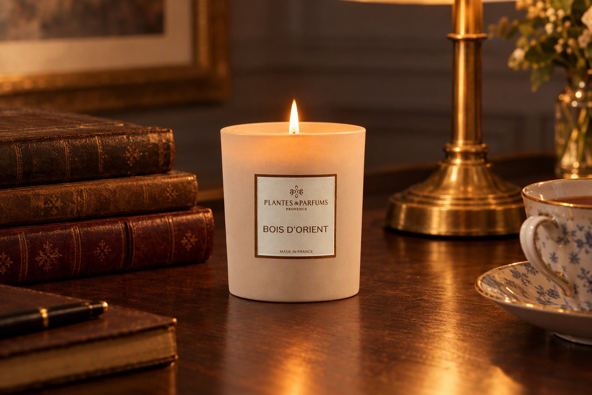 Bougie Bois d'Orient allumée sur un bureau en bois sombre avec des livres et une lampe