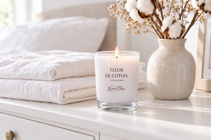Bougie Fleur de coton allumée sur une commode blanche avec du linge plié et des fleurs de coton