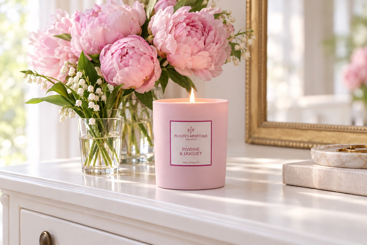 Bougie Pivoine et muguet allumée à côté d'un bouquet de pivoines roses et de brins de muguet