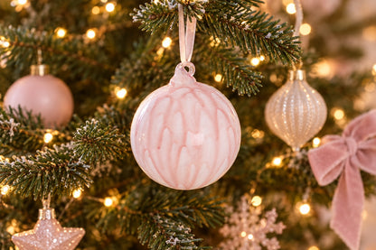 Boule de Noël en verre rose et blanc suspendue à une branche de sapin