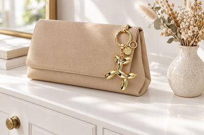 Charm chien ballon doré accroché à une pochette beige sur une commode