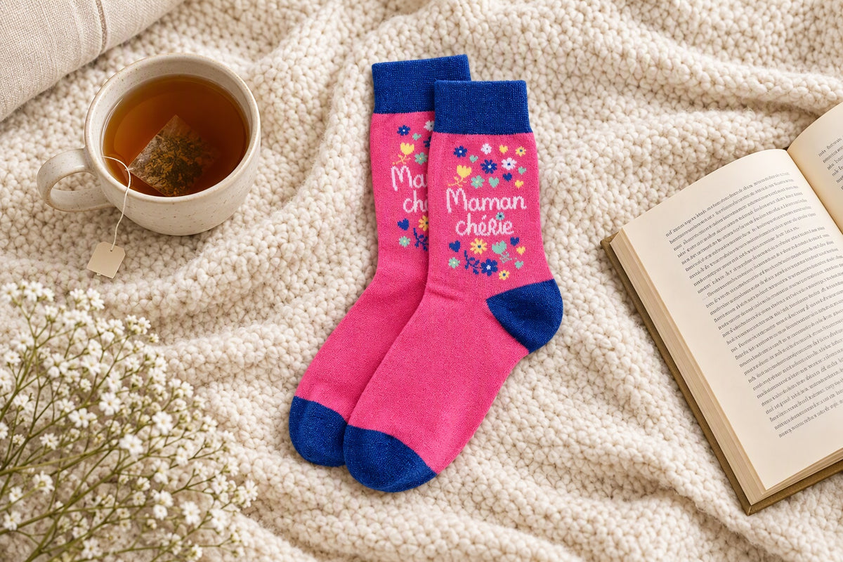 Chaussettes Maman chérie rose et bleu posées sur un plaid avec une tasse de thé