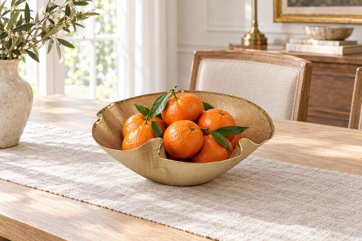 Coupe en verre ondulée dorée remplie de clémentines sur une table à manger