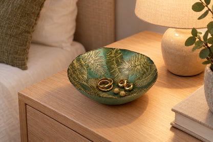 Coupelle en verre verte à feuilles dorées avec des bijoux sur une table de chevet