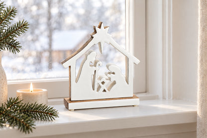 Crèche de Noël sur socle en bois naturel et blanc posée sur un rebord de fenêtre avec une petite bougie