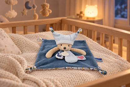 Doudou ourson bleu plat posé sur une couverture tricot dans un berceau en bois