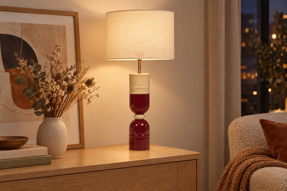 Lampe à poser crème et bordeaux allumée sur une console dans un salon