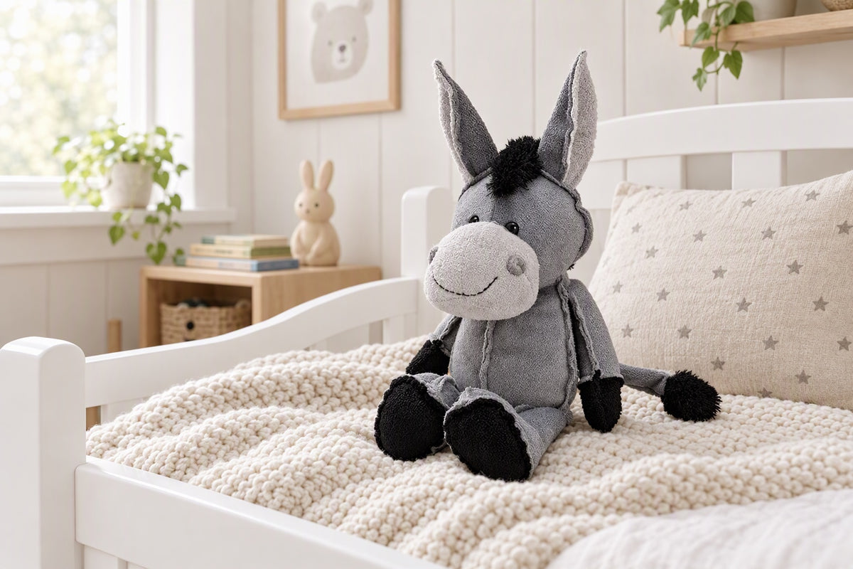 Peluche âne grise assise sur un lit d'enfant avec un coussin