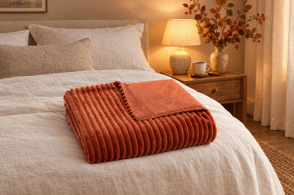 Plaid terracotta plié au pied d'un lit en lin dans une chambre chaleureuse d'automne