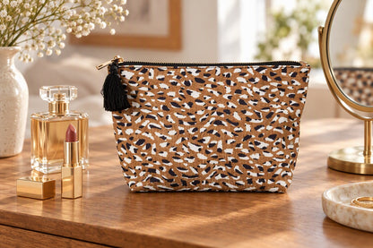 Pochette léopard avec pompon noir posée sur une coiffeuse avec rouge à lèvres et parfum