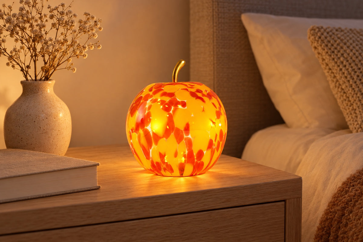 Pomme lumineuse en verre jaune et orange allumée sur une table de chevet