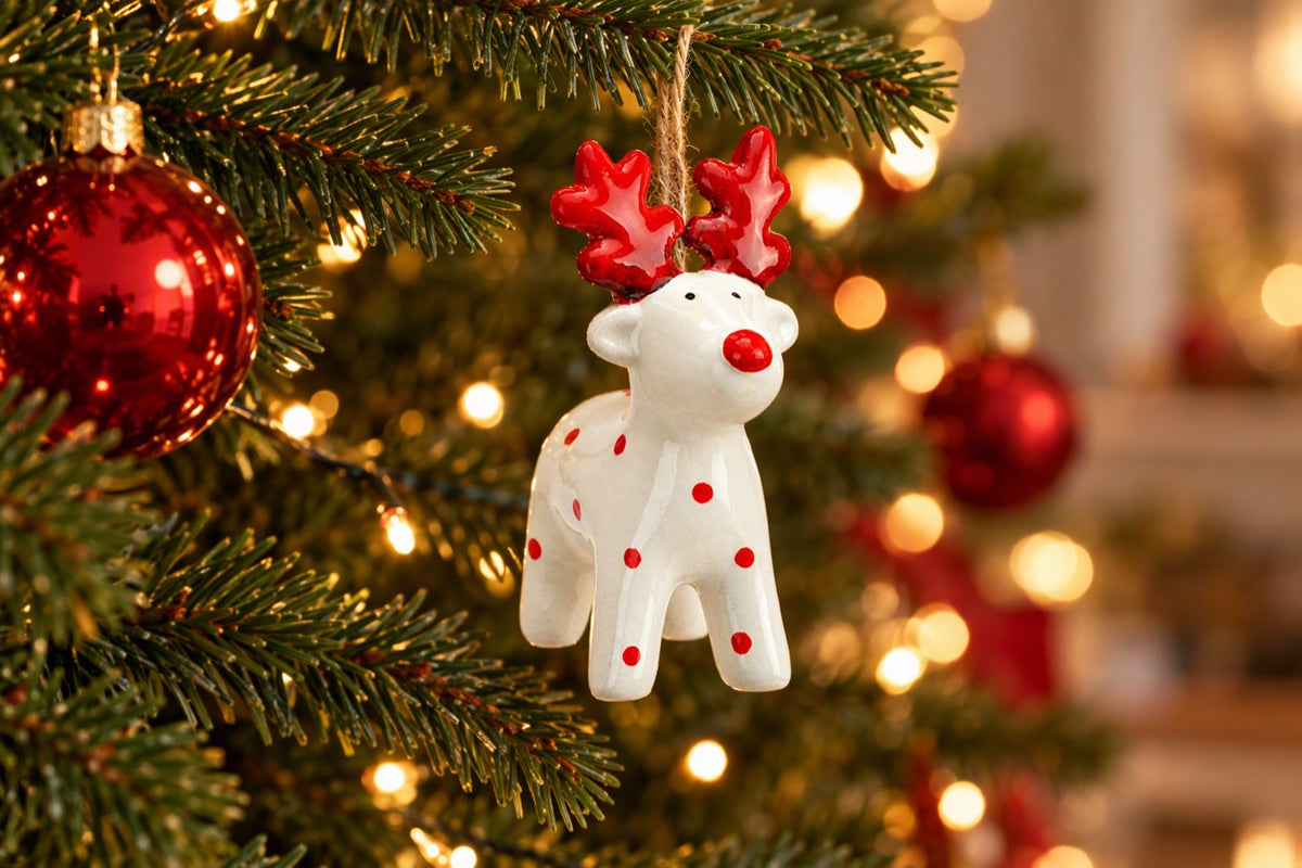 Suspension de Noël cerf blanc et rouge accrochée à une branche de sapin avec guirlande lumineuse
