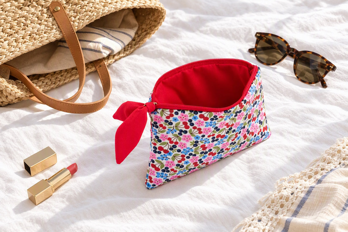 Trousse plate imprimé cerises avec nœud rouge posée sur un lit à côté d'un sac à main