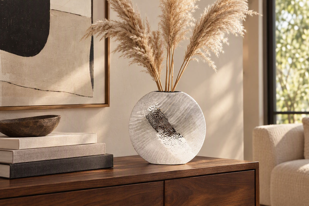 Vase rond argenté en aluminium martelé avec des tiges de pampa sur un buffet