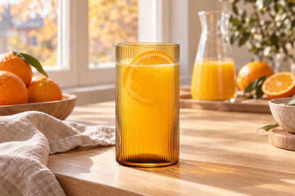 Verre orangeade ambre strié rempli de jus d'orange sur une table de cuisine en bois au petit-déjeuner
